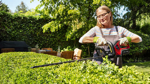 Žena upravuje živý plot pomocou akumulátorového plotostrihu Honda v záhrade.