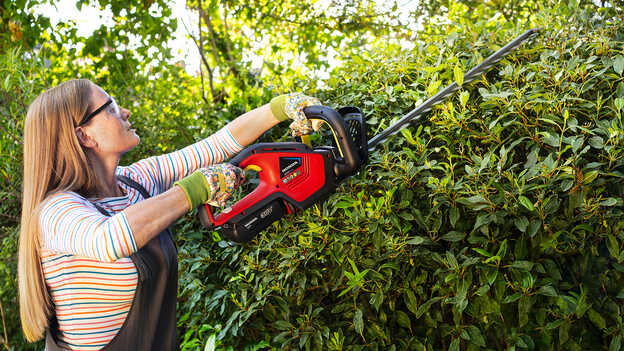 Žena upravuje kríky pomocou akumulátorového plotostrihu Honda v záhrade.